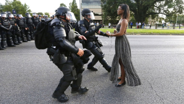 A woman stands calming in front of police officers in riot gear.